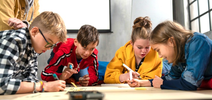 AJ-01-makerspaces-720 | MiddleWeb Four children collaborating on a project at a low table, drawing and writing with markers in a bright room,